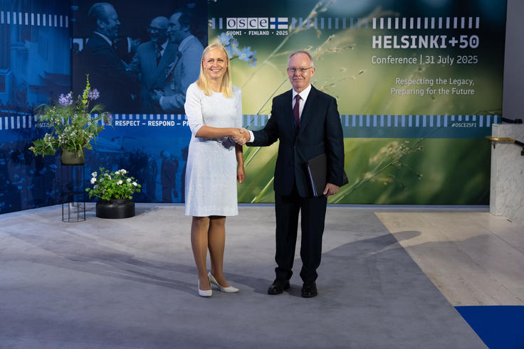 OSCE Representative on Freedom of the Media, Ambassador Jan Braathu, with Minister of Foreign Affairs of Finland, Elina Valtonen, shaking hands in front of a banner showing the logo of the Helsinki+50 Conference, smiling, with the Ambassador holding a folder with documents.